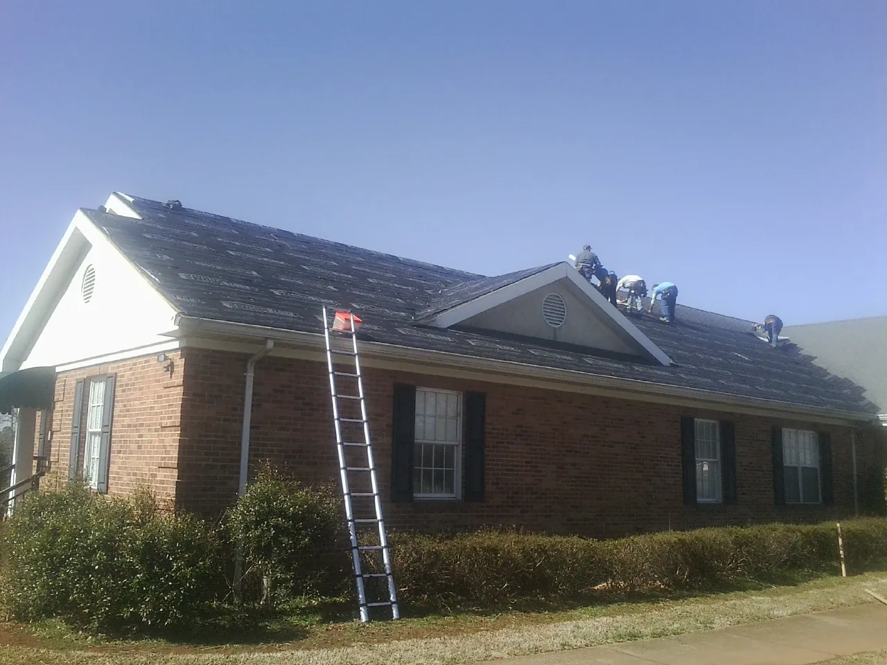 Crew tearing shingles off a brick ranch roof with a ladder set — Emergency Roof Repair work by our crew in Cocoa
