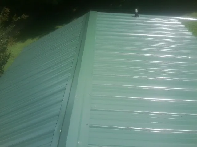 New green metal panels meeting at the ridge of a roof — Flat Roof Repair work by our crew in Cocoa