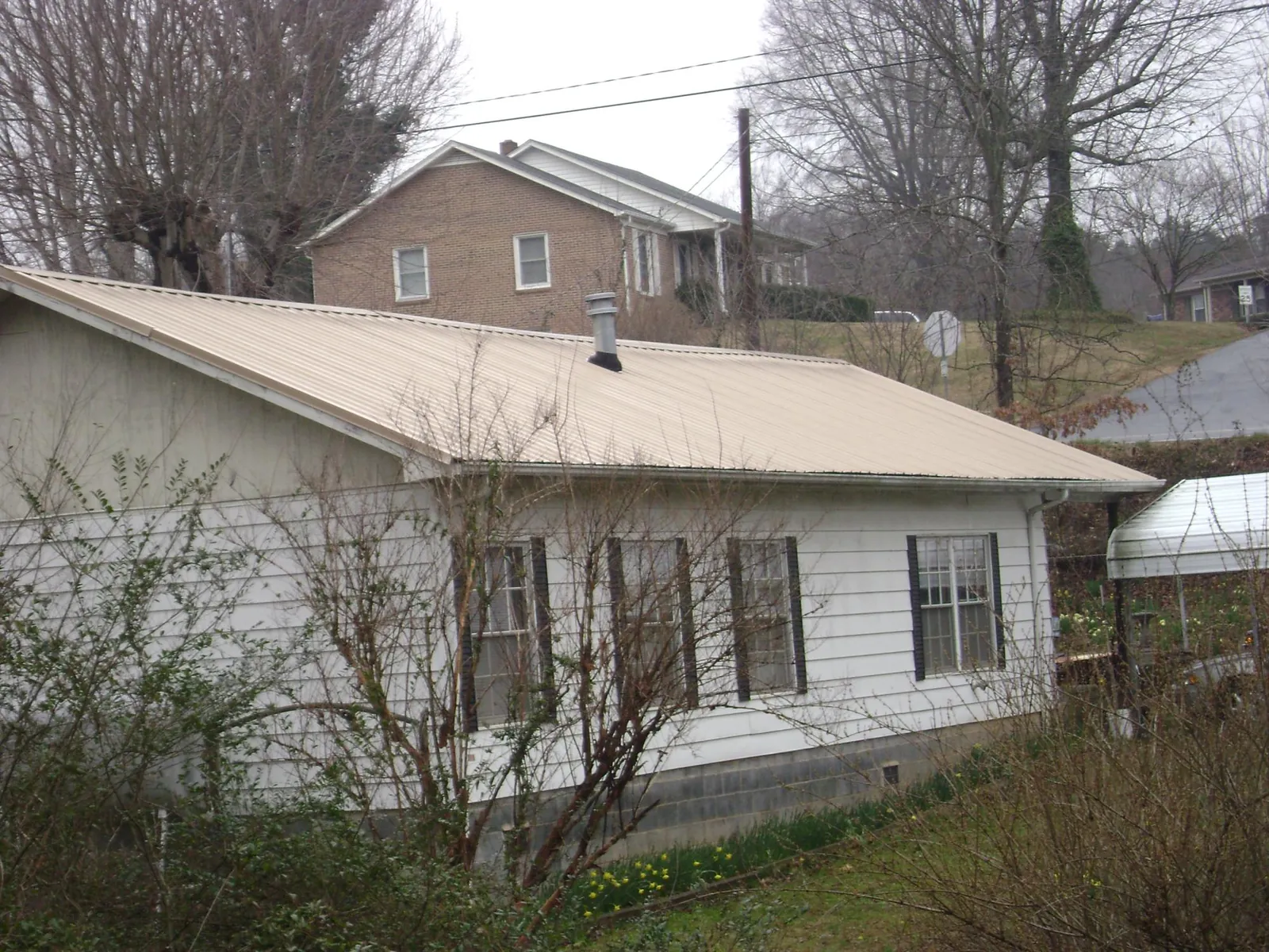 Tan metal roof on a white sided house set into a hillside — Commercial Roofing by Roofing Brothers in Cocoa