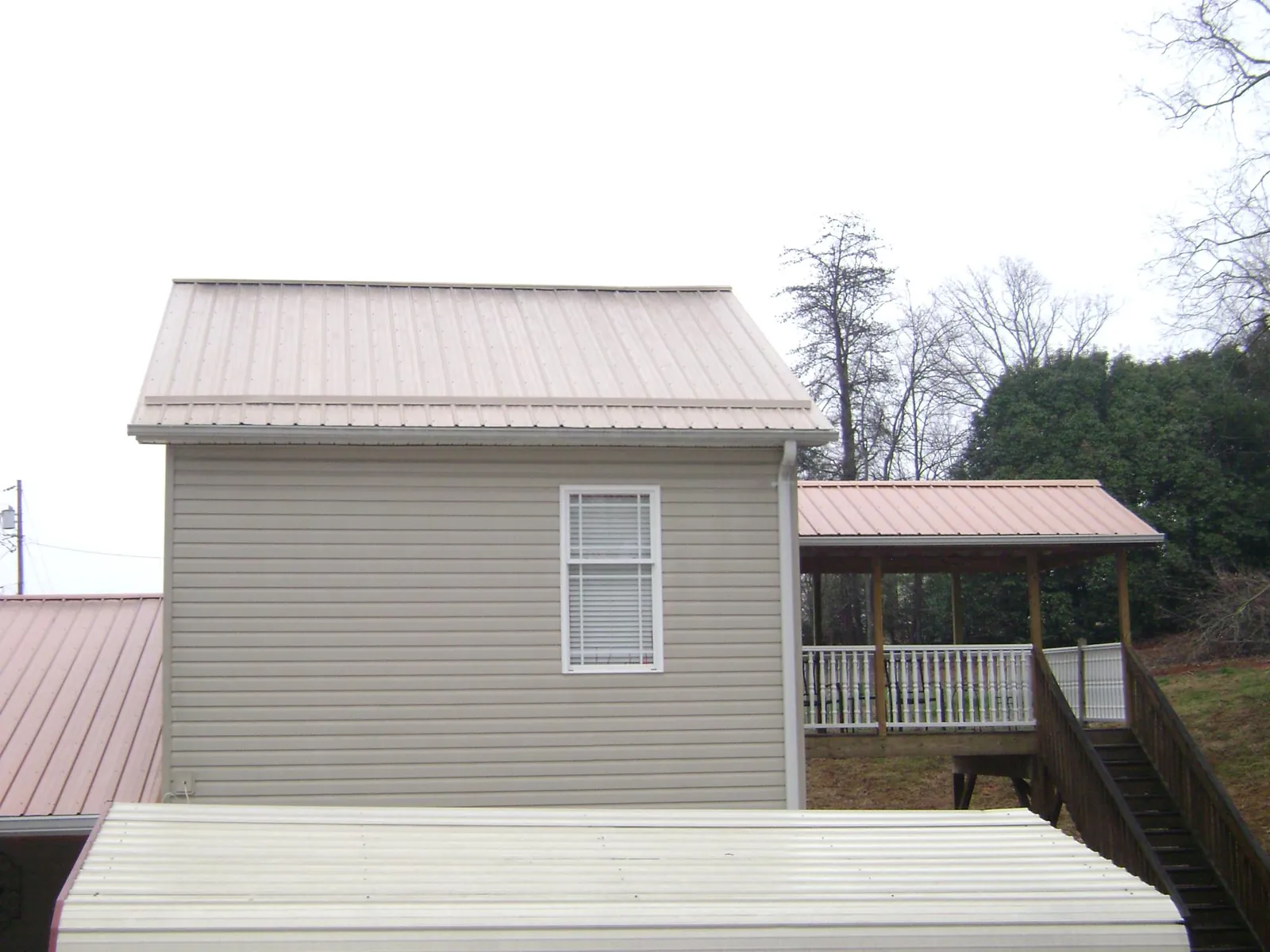 Tan metal roofs on a two story addition and attached porch, from a Roof Replacement job in Cocoa